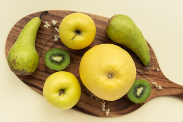 A variety of yellow and green fresh fruit on a wooden board on a yellow background shot from above
