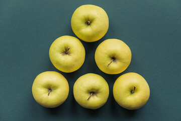 golden delicious apples set in an triangle on a green background
