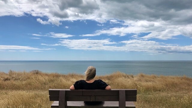 Rear view of a woman sitting on a bench looking at view, Barton on Sea, Hampshire, England, UK