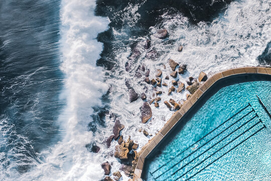 Aerial View Of Large Ocean Waves Breaking Towards Natural Water Coastal Swimming Pool With Person Swimming In Bronte, Sydney, Australia