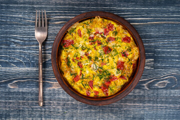 Ceramic bowl with vegetable frittata, simple vegetarian food. Frittata with tomato, pepper, onion and cheese on wooden table, close up