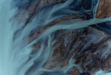 Aerial view of beautiful blue patterns, and swans swimming in the water of glacial river H√©raosvotn in North Iceland.