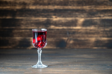 Homemade tincture of red cherry in a wine crystal glass on wooden background, Ukraine