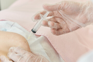 Doctor gloved hand makes an injection with plastic syringe to patient, needle is inserted under skin.