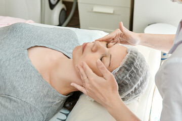 Hands of beautician are doing massage on the face of young woman.