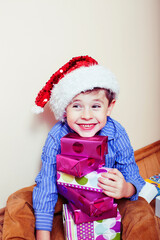 little cute boy with Christmas gifts at home wearing red Santas hat. closeup emotional happy smiling in mess with toys, lifestyle holiday people concept