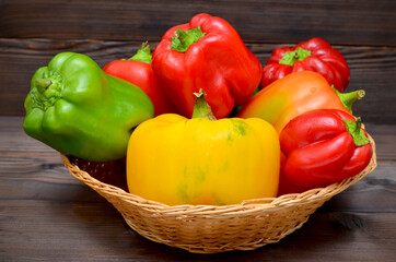 appetizing green and red and yellow peppers in basket on a wooden background 