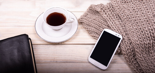 Cup of coffee, cellphone, 
book and blanket on wooden table.
 holiday home decor concept.