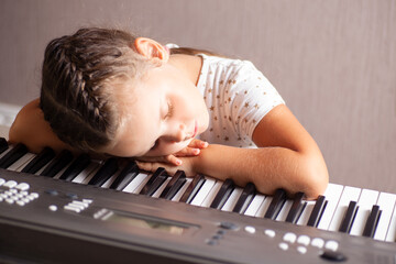 a child, a girl in a white dress sleeping on the keys of an electronic piano, synthesizer, close up.