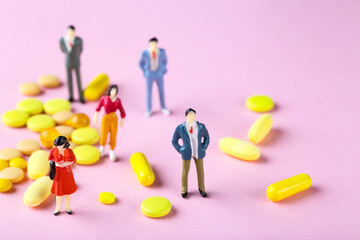 Miniature people with pills on pink background