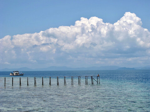 Looking out at the clear waters and a distant dock, with a single person sitting at the end, at Sipadan Island, Sabah, Malaysia © Jen