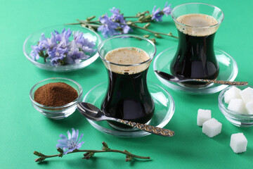 Obraz na płótnie Canvas Chicory beverage in two glass cups, with concentrate and flowers on green background. Healthy herbal beverage, coffee substitute, Closeup