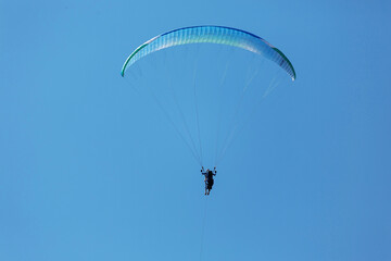 Blue Paraglider flying into the sky with clouds on a sunny day