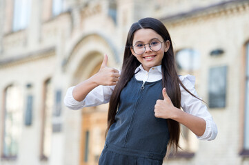 Happy child in school uniform give thumbs ups hand gesture in schoolyard outdoors, approval. good education