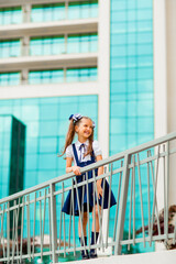A schoolgirl in a blue school uniform, standing in the background of the school, with glass walls.