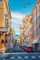 Fototapeta premium Typical italian street with parked cars and Torre della Pallata brick medieval tower building background, Brescia city historical centre, vertical view, Lombardy, Northern Italy