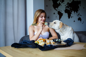 Beautiful blonde woman eating sushi close-up with her labrador dog, Smiling woman with lovely makeup holding a sushi roll with chopsticks. Healthy Japanese food. Diet concept