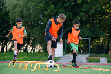 Active teen footballers train together on artificial soccer field and follow the instructions of a...