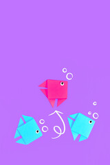Bright pink paper fish swimming out of line of blue fish on purple background. Concept for new business strategies, discovery, and different thinking