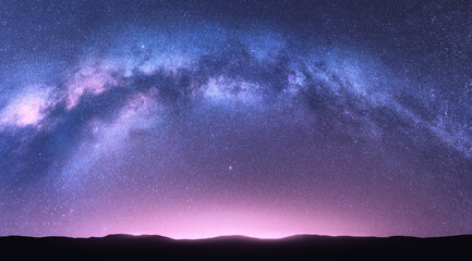 Milky Way arch. Fantastic night landscape with bright arched milky way, purple sky with stars, pink light and hills. Beautiful scene with universe. Space background with starry sky. Galaxy and nature - 374986785