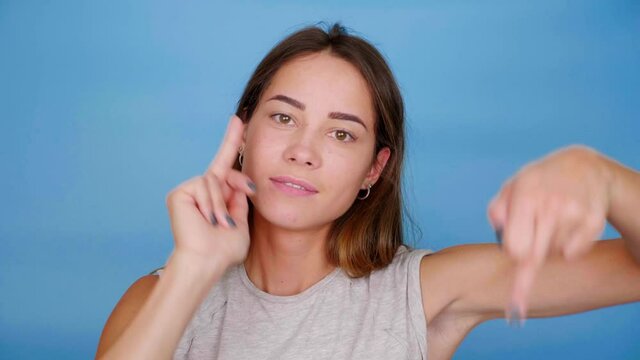 Funny woman in gray t-shirt smiles, dances, shows middle finger on blue background with copy space. 4K slow motion footage