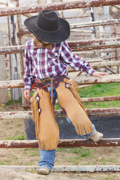 Young cowboy leaning against corral fence.