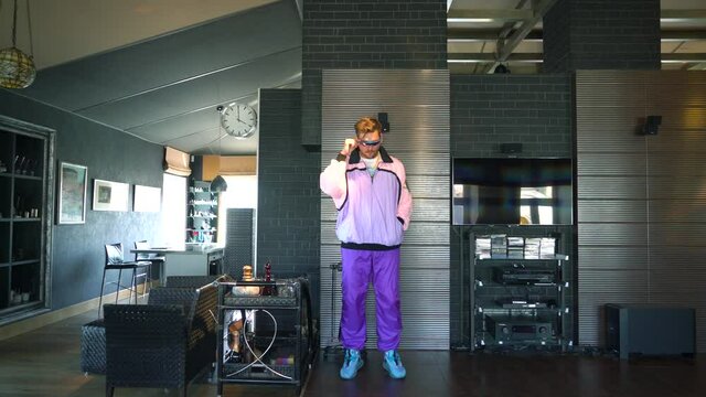 A freak guy in a fashionable suit from the 80s and 90s is dancing at home and grimacing at the camera, a funny cheerful young man, he is filming for social networks, handsome gay, colored clothes.