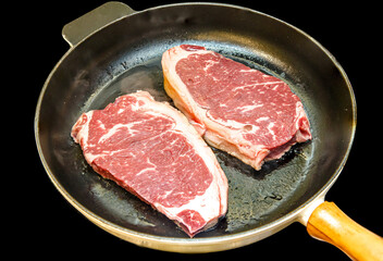 Striploin steak (new York) of marbled beef is fried in a black pan