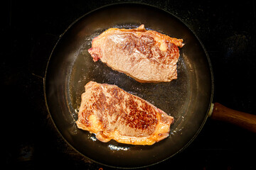 Striploin steak (new York) of marbled beef is fried in a black pan