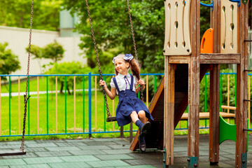 schoolgirl in school uniform, swinging on a swing in a children's Park