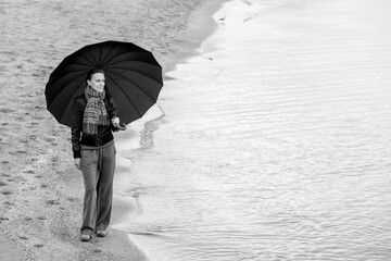 woman with umbrella in winter or autumn walking near sea	