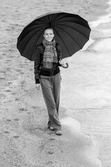 woman with umbrella in winter or autumn walking near sea	