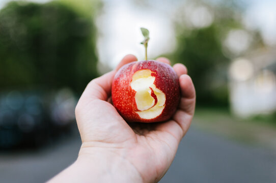 Hand holding a red apple minus a bite