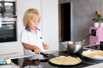 Cute toddler child, blond boy, making pancake in kitchen