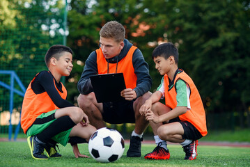 Professional soccer coach tells the strategy of football game to his attentive teen players at stadium during training. - obrazy, fototapety, plakaty