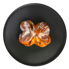 Isolate of a round black dish with a sweet bun with raisins. Top covered with white glaze. View from above