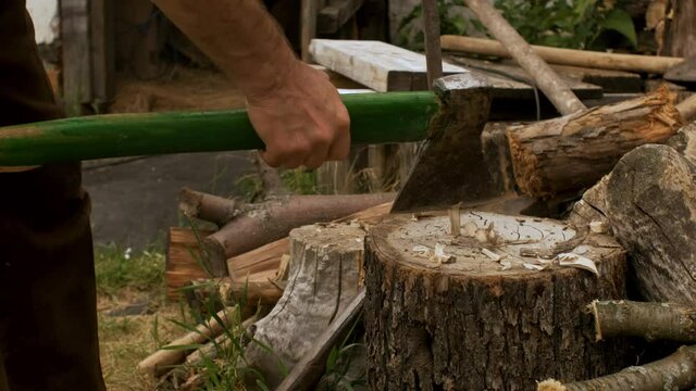 A rural man cuts wood with an axe and makes a peg for construction. Close up