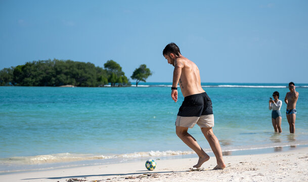 Young man plays with the ball on the beach of Koh Samui, Thailand, in the background of tourists take a picture of him.