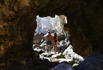 A half-naked man and woman emerge from the cave onto the rocky shore of the ocean. Couple in love.
