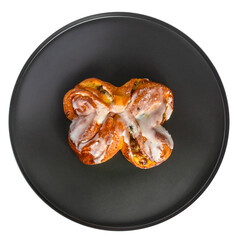 Isolate of a round black dish with a sweet bun with raisins. Top covered with white glaze. View from above