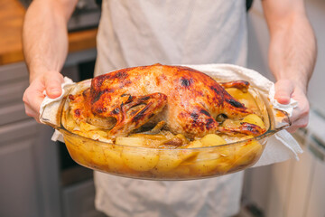 Duck with potatoes baked in the oven in the hands of a man in an apron