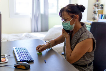 Woman working on her computer from home while she is wearing preventive mask
