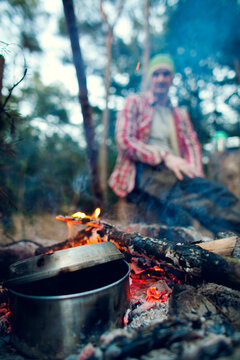 Young man sitting next to a campfire cooking dinner