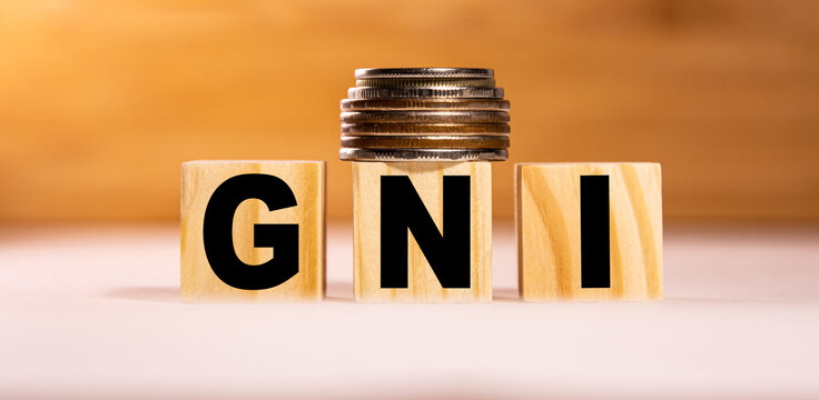 The concept of the word gni on wooden cubes with coins on a white wooden background. Business concept. GNI Gross national income