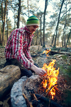 Young man sitting next to a campfire in a forest
