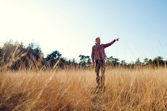 Man standing in high grass pointing at something