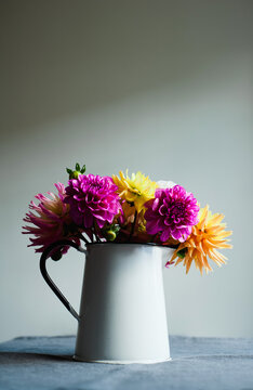 Brightly coloured Dahlias in an enamelware vase on a tablecloth