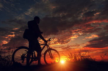 Obraz premium cyclist with a bicycle, in the background fiery sunset.