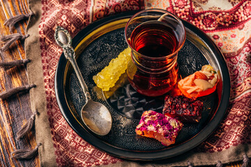Tea in armudu glass with oriental delight rahat lokum on metal tray over wooden surface and tablecloth