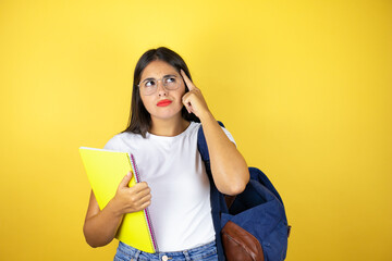 Young beautiful student woman wearing backpack holding notebook over isolated yellow background smiling and thinking with her finger on her head that she has an idea.